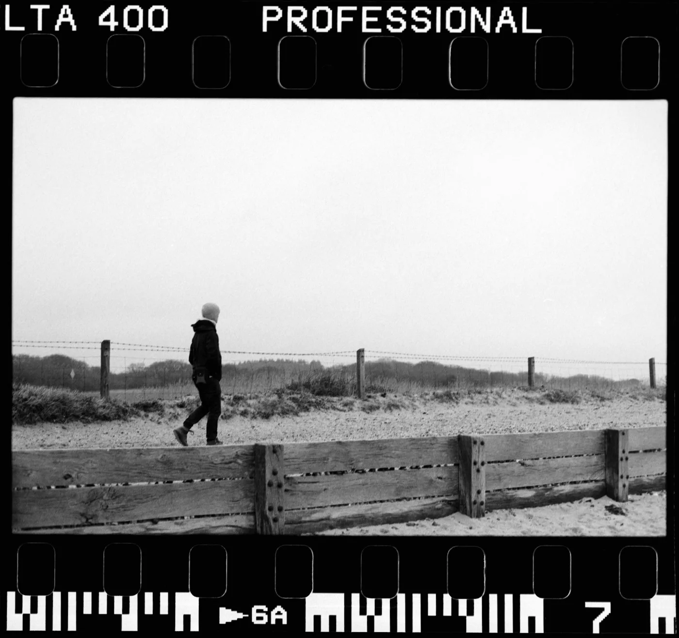 Grainy black and white photograph of a person walking near the sea