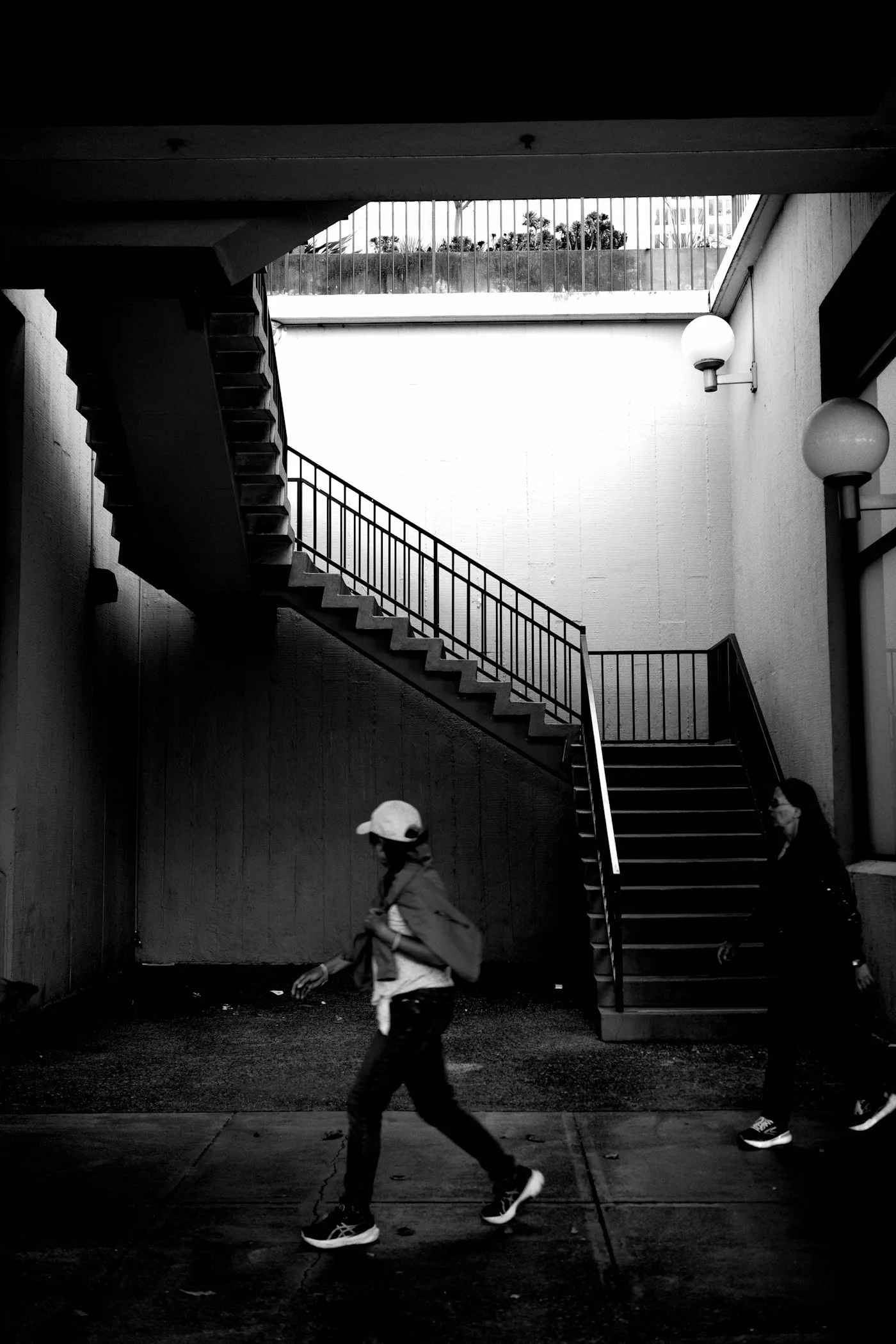 People walking past an angular staircase in black and white